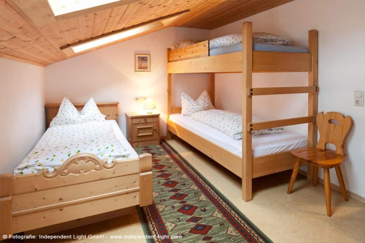 Une chambre avec deux lits superposés, une chaise en bois, une table de chevet et un tapis à motifs.