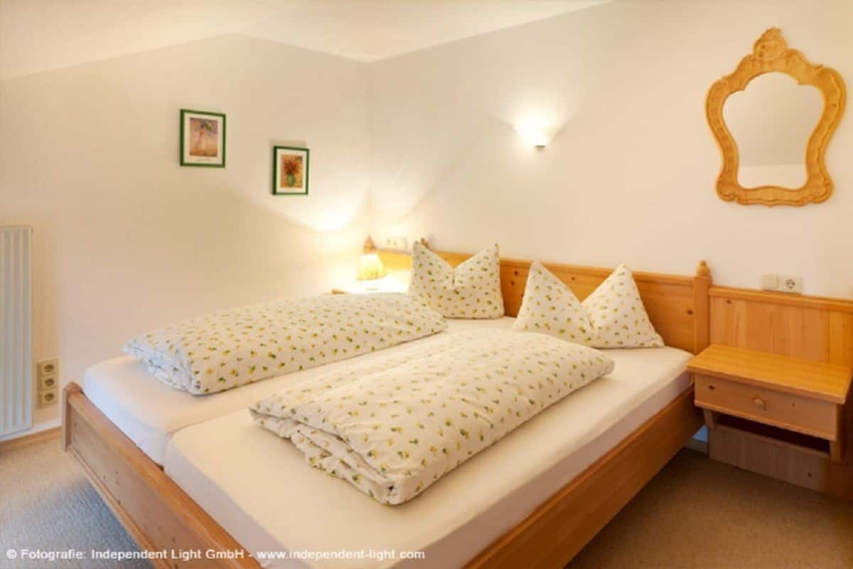Un lit double avec une tête de lit en bois, deux tables de chevet et une petite table de nuit. Deux tableaux encadrés sont accrochés au mur.