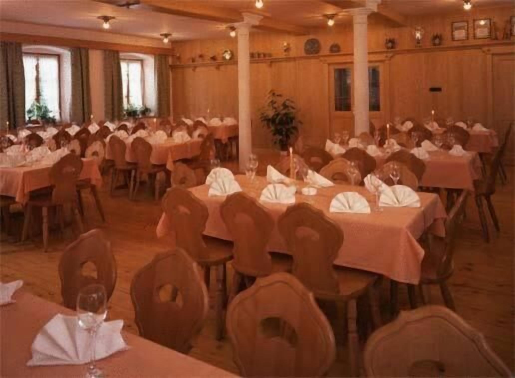 Un salón de banquetes con varias mesas redondas dispuestas para el servicio de comidas, cada una con manteles blancos y servilletas dobladas.