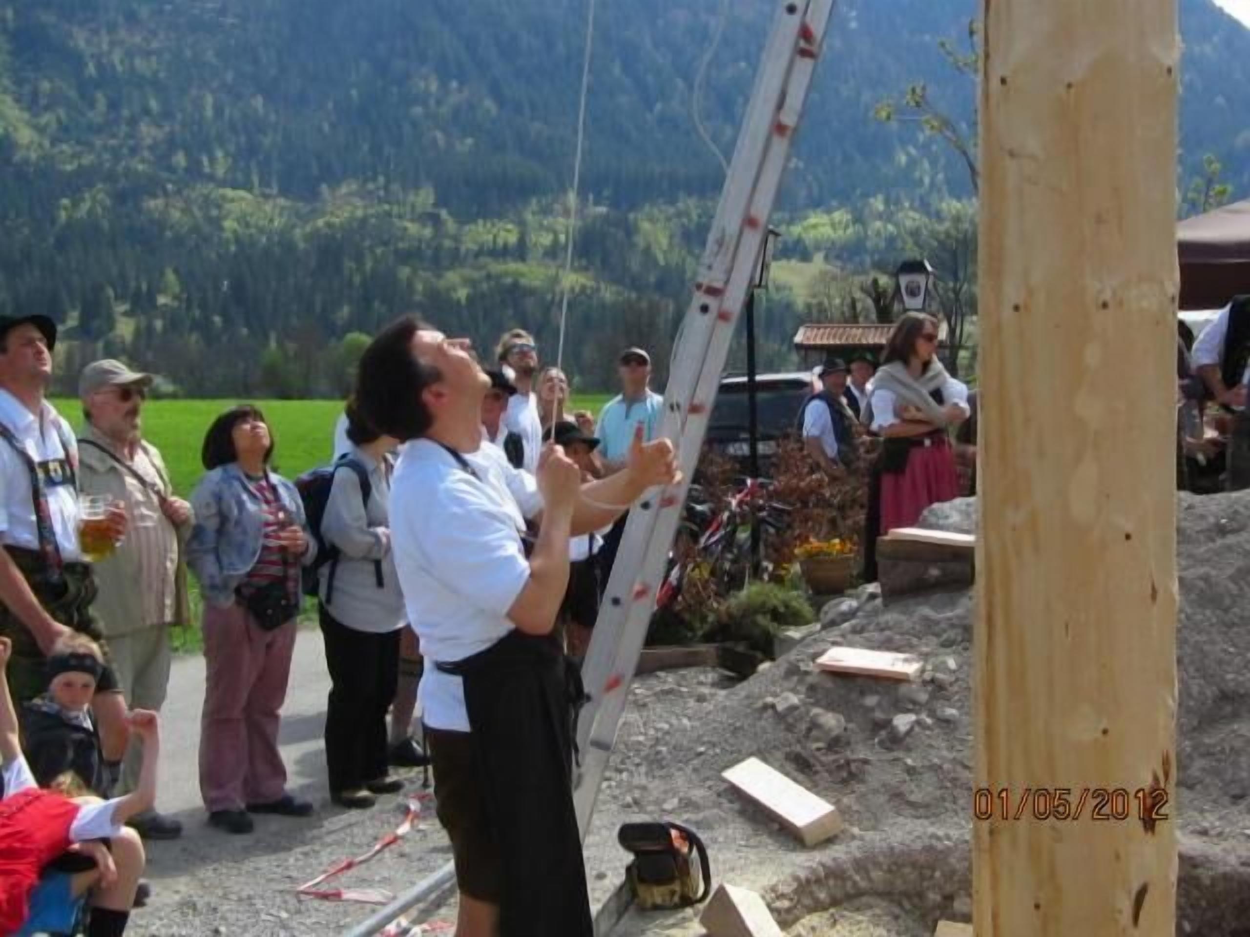 A group of people outdoors, some standing and some sitting, with a mountainous background.