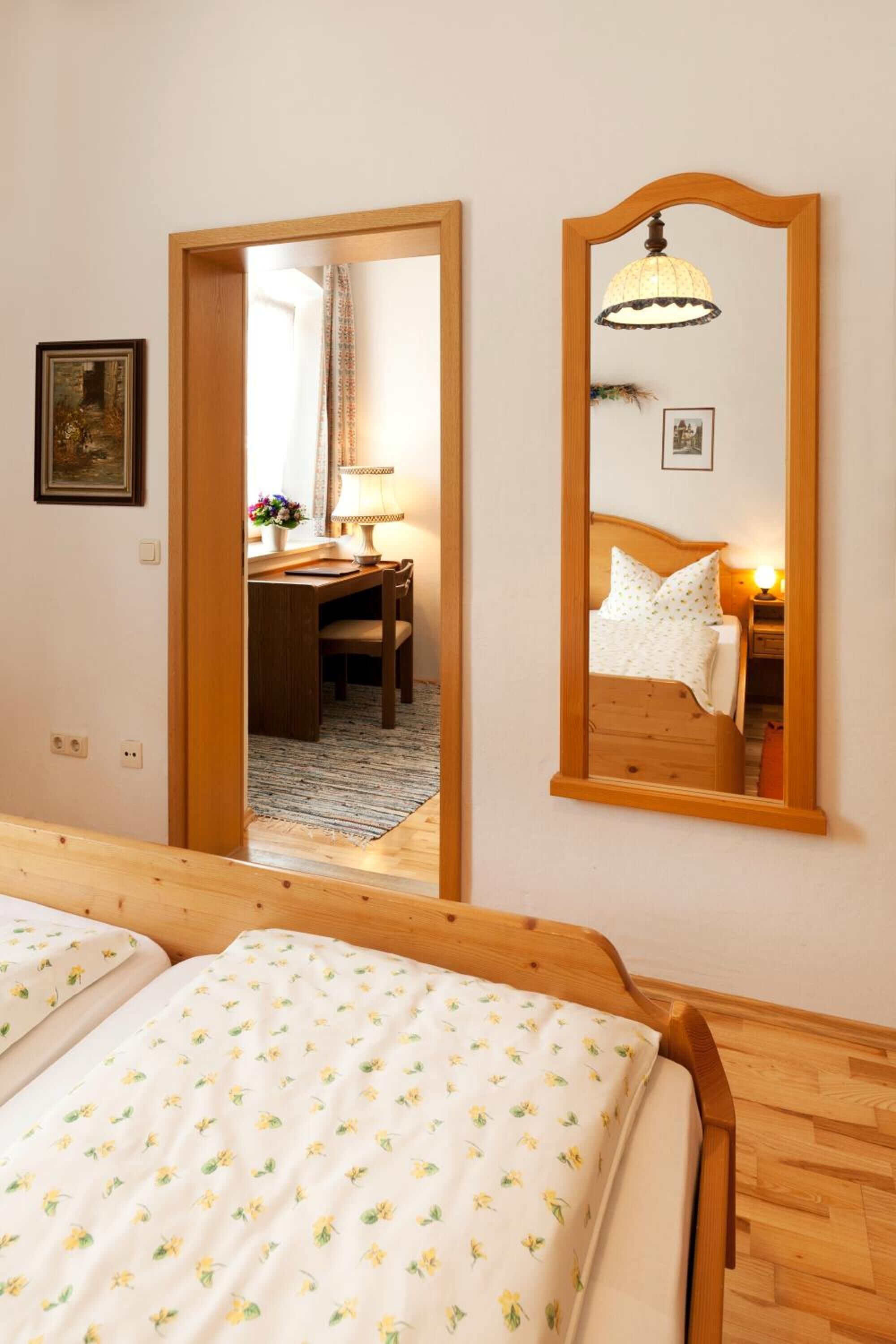 A bedroom with a wooden bed, a mirror, and a desk with a lamp.