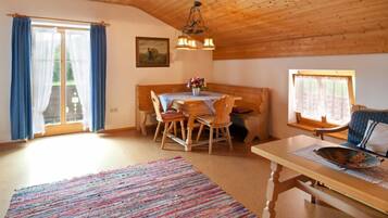 A cozy room with a wooden ceiling, a dining table with chairs, a bench, a sofa, and a large rug.
