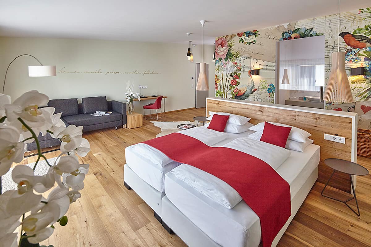 A modern hotel room with a large bed, a desk, and a sofa.