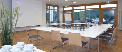 A conference room with a long table, chairs, a whiteboard, and a view of parked cars outside.
