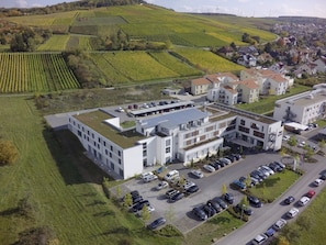 A modern hotel with a flat roof, multiple parking spaces, and a view of vineyards in the background. - Hotel Kapellenberg (Eibelstadt)