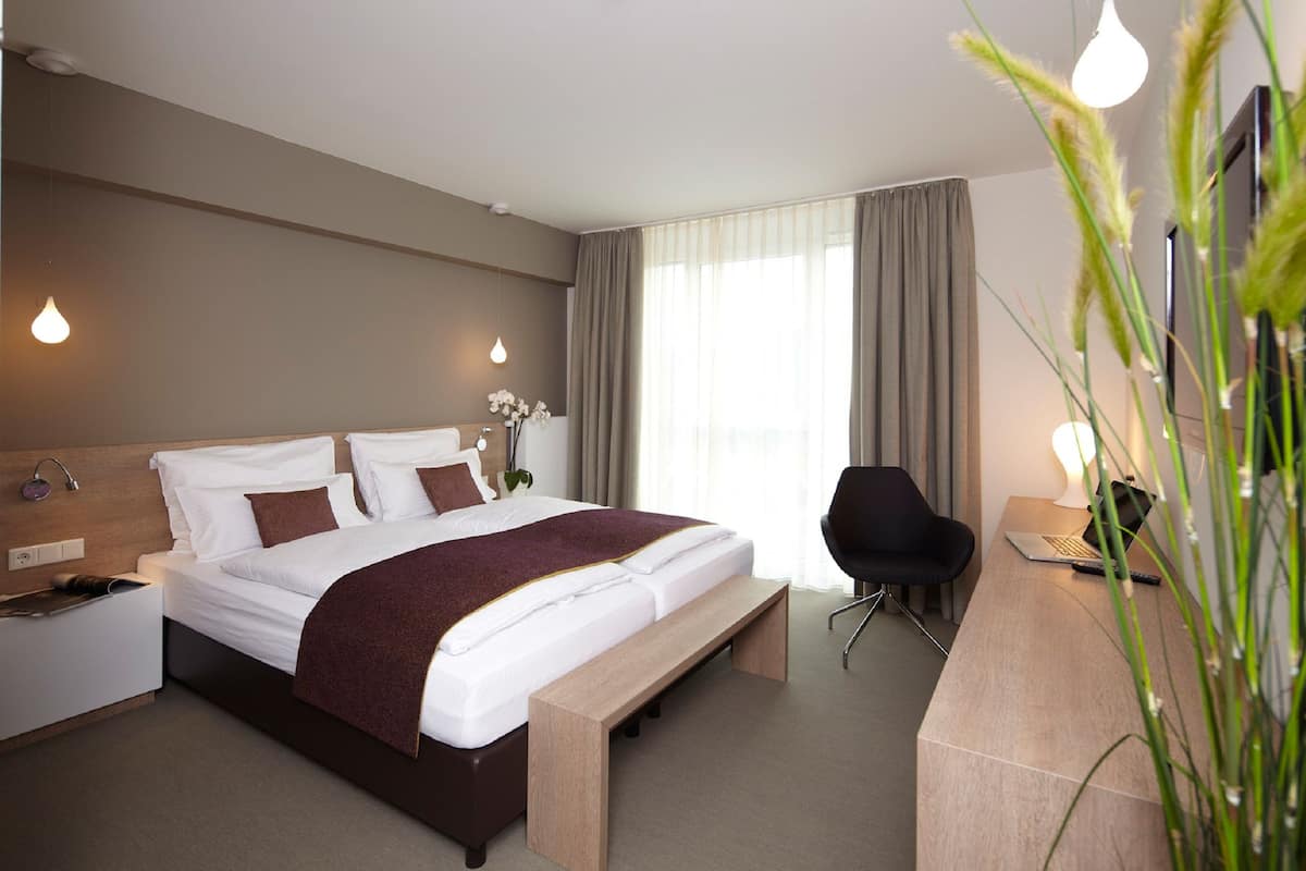 A modern hotel room with a large bed, bedside tables, a desk, and a chair.