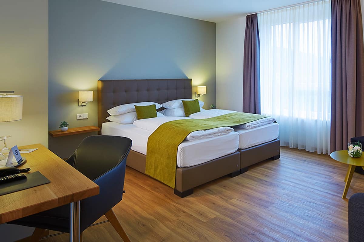 A hotel room with a bed, a desk, a chair, a small table, and a sofa.