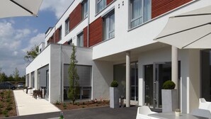 A modern building with a flat roof, large windows, and a covered outdoor seating area with white tables and chairs. - Hotel Kapellenberg (Eibelstadt)