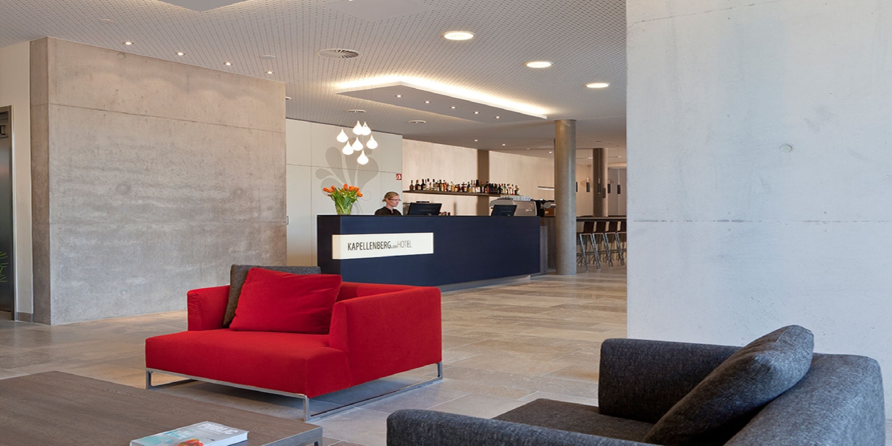Un moderno vestíbulo de hotel con una recepción, un sofá rojo y una zona de bar.