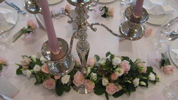 Une table dressée pour un événement formel, avec des couverts en argent, des assiettes et des bougies roses.