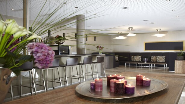 A modern bar area with a round wooden table, bar stools, and candles. - Hotel Kapellenberg (Eibelstadt)