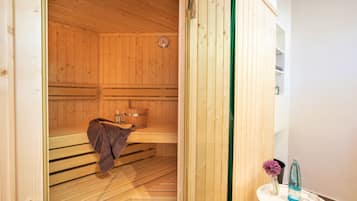 Uma sauna com bancos de madeira, uma toalha, um balde e um relógio na parede.