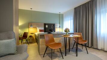 Una habitación de hotel con una cama, un escritorio, dos sillas, una lámpara y un florero con flores.