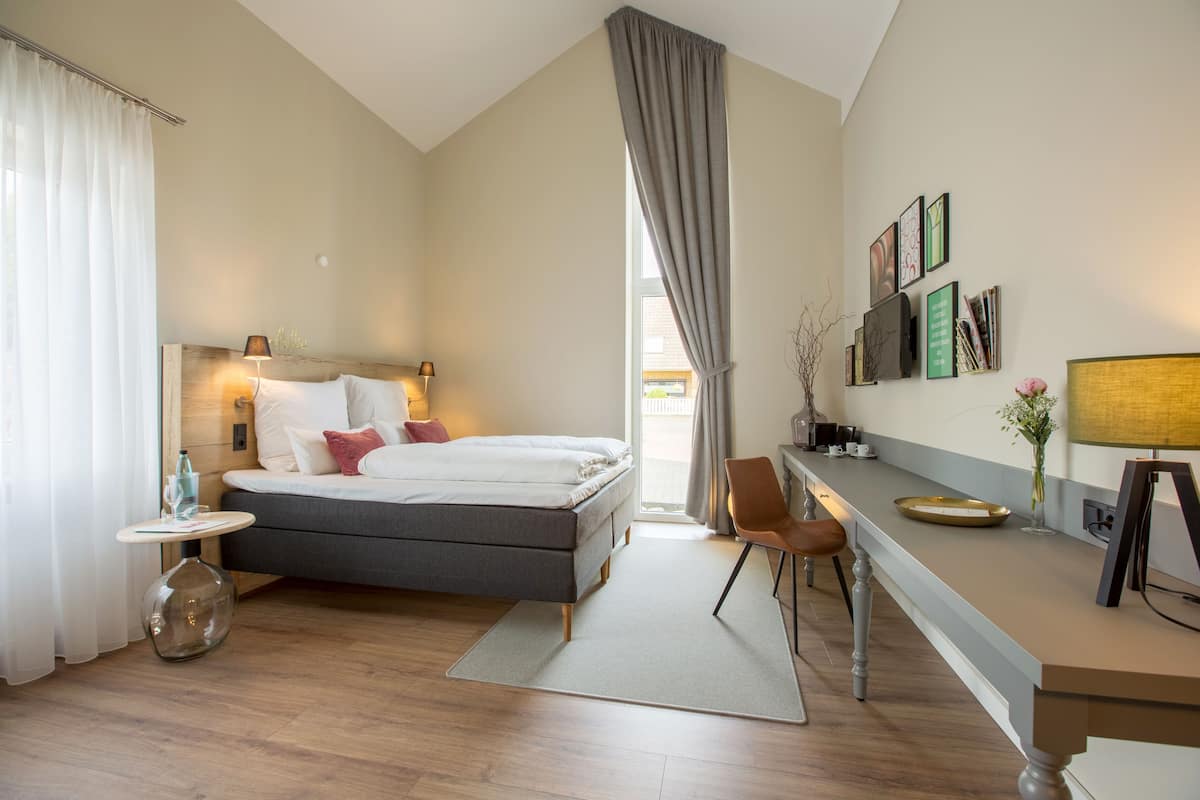 Une chambre d’hôtel moderne équipée d’un lit, d’une table de chevet, d’une lampe et d’un bureau avec une chaise.
