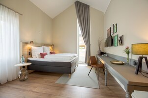 Ein modernes Hotelzimmer mit Bett, Nachttisch, Lampe und Schreibtisch mit Stuhl.