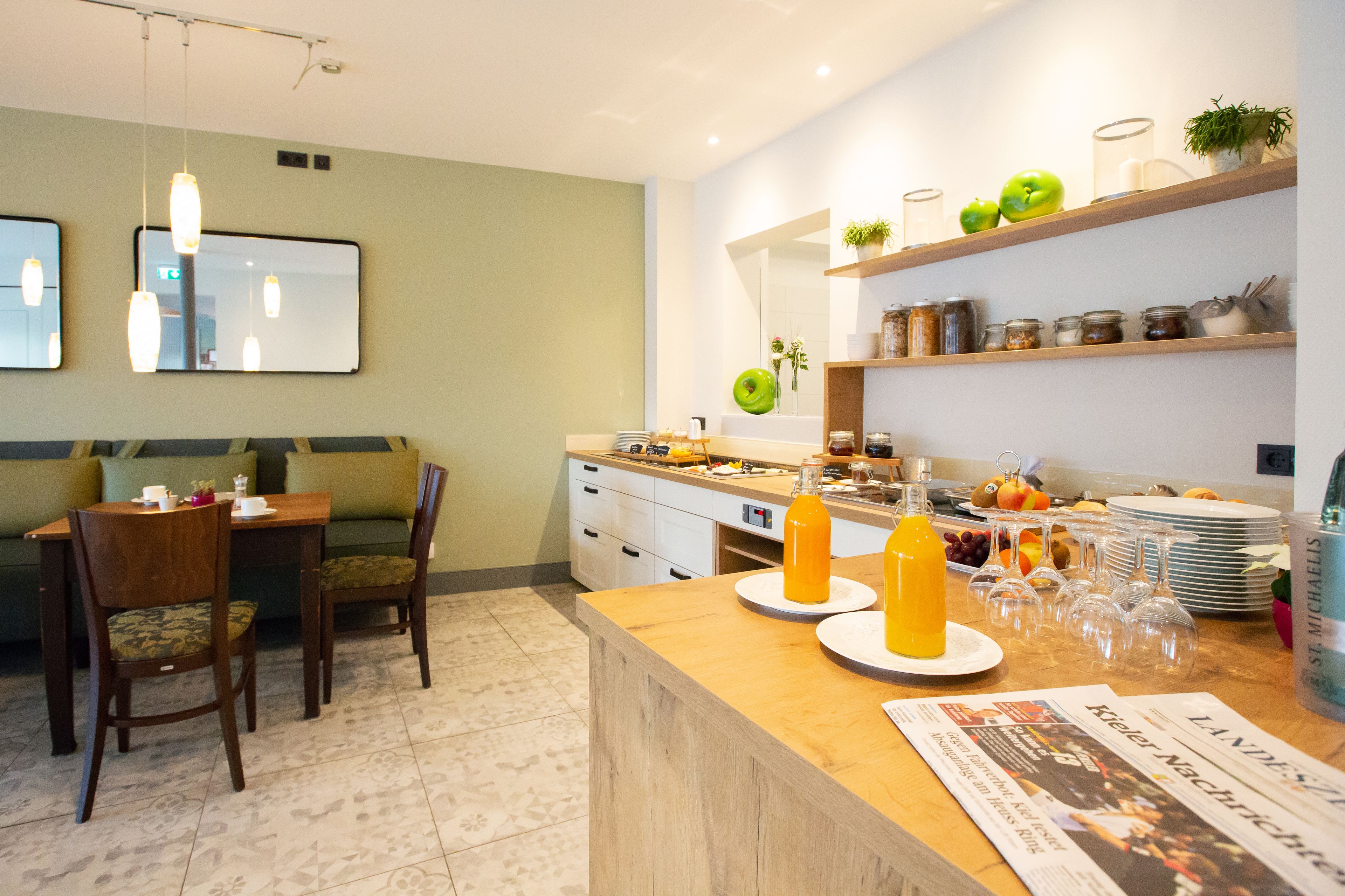 Une cuisine moderne avec un coin repas, comprenant une table en bois, des chaises, un comptoir avec de la verrerie et une étagère avec des bocaux et des pommes.
