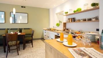 Une cuisine moderne avec un coin repas, comprenant une table en bois, des chaises, un comptoir avec de la verrerie et une étagère avec des bocaux et des pommes.