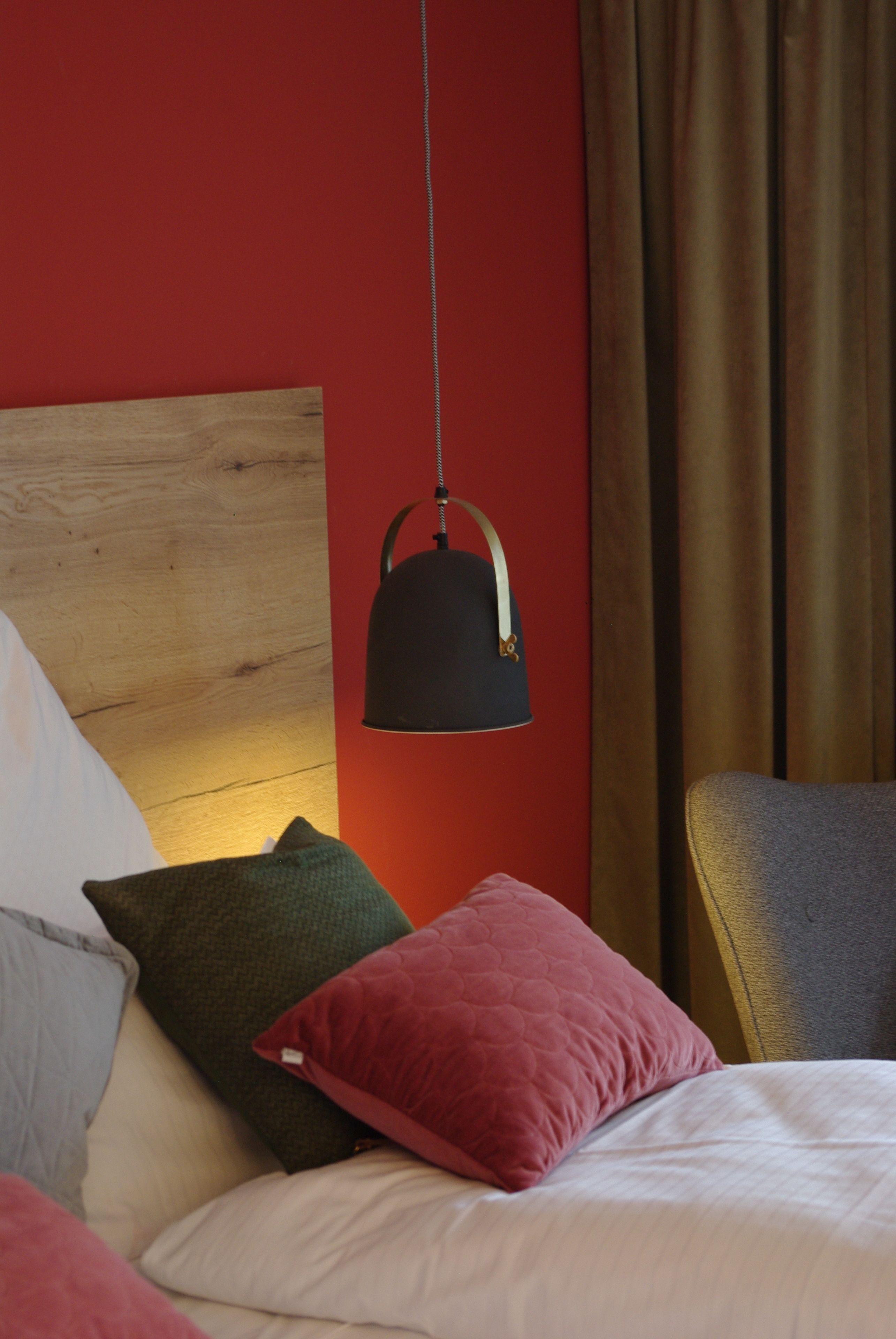 Una cama con varias almohadas, una lámpara colgante y un cabecero de madera en una habitación con paredes rojas y una cortina.