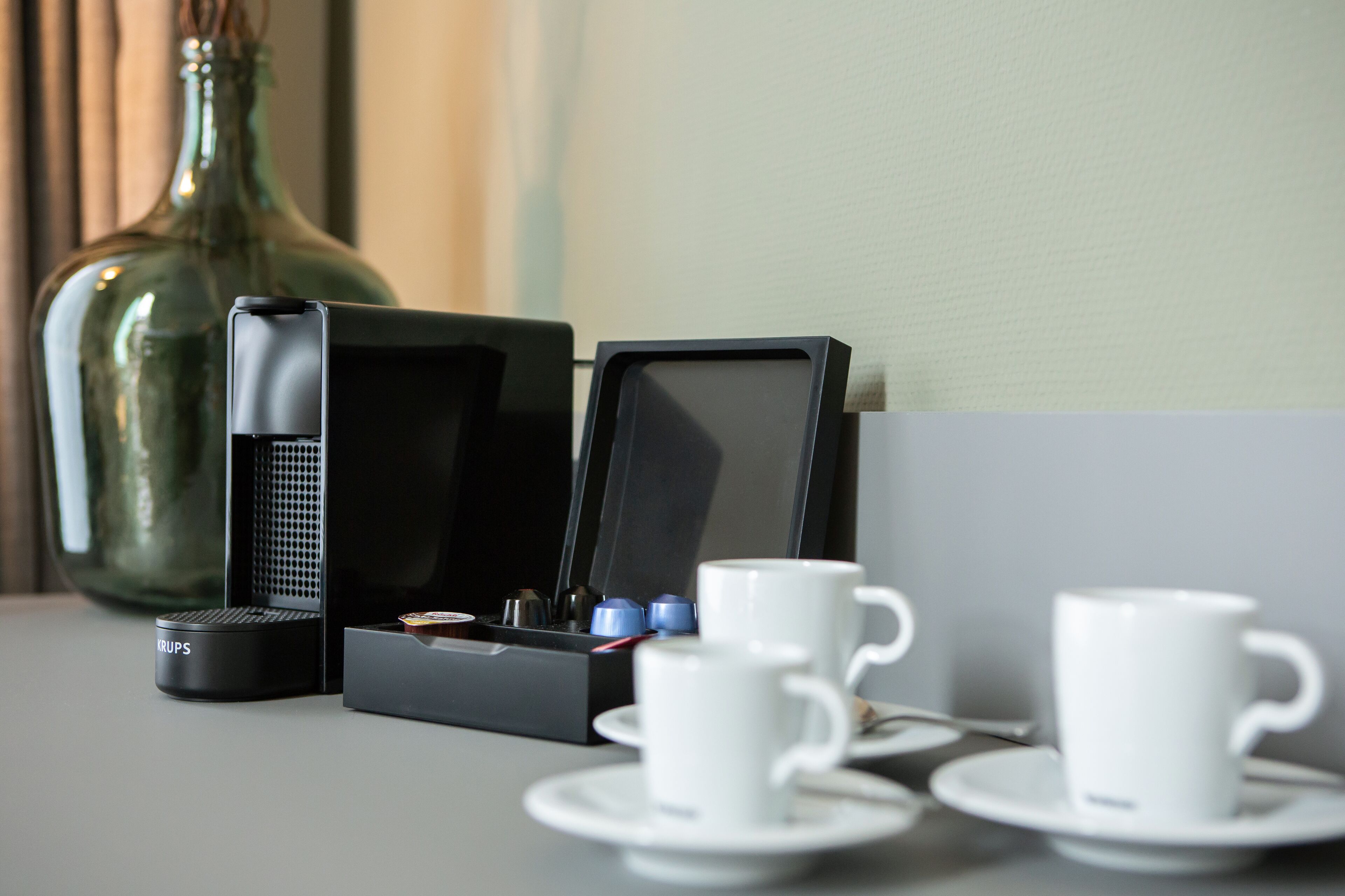 A coffee machine, two cups, and a vase on a table.