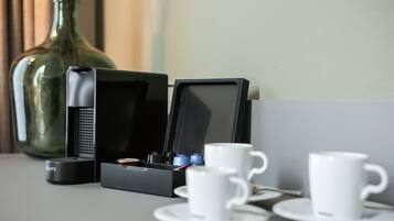 A coffee machine, two cups, and a vase on a table.