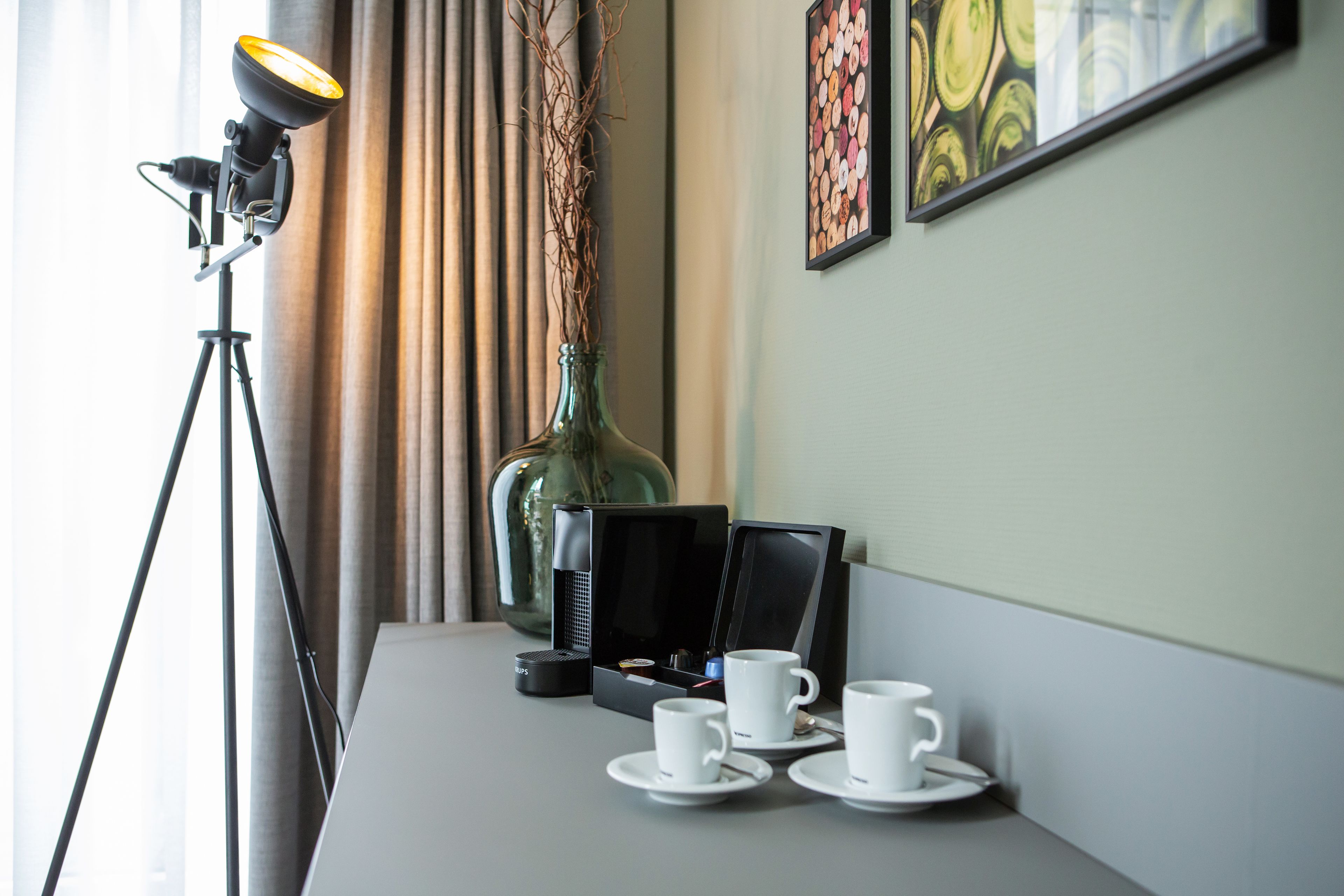 A table with a lamp, a bottle, a coffee maker, and three cups.