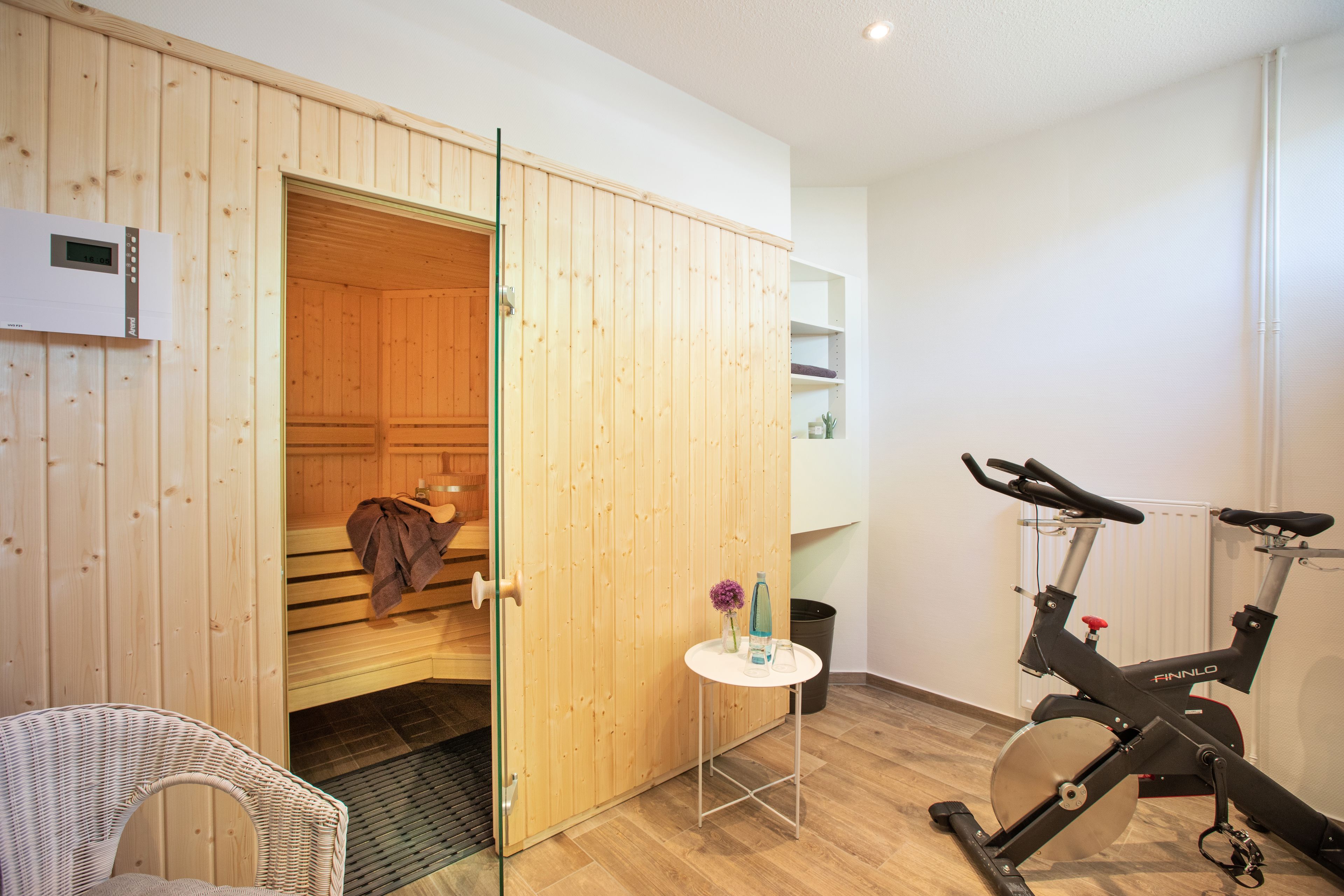 Una habitación con sauna, camilla de masaje, sillón de masajes, una mesita con un jarrón y una bicicleta estática.