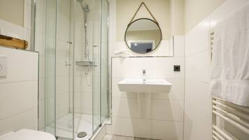 A modern bathroom with a glass-enclosed shower, a white sink, and a towel rack.
