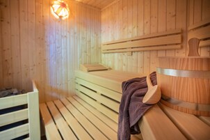 Ein Raum mit einer Holzzauna, Bänken und einem Holzwascheimer.