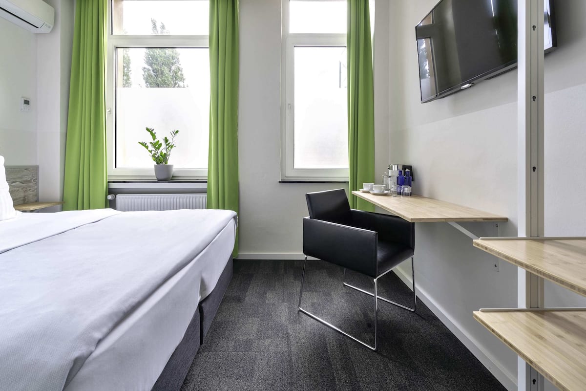 Une chambre d’hôtel avec un lit, un bureau et une chaise, une télévision et une fenêtre avec des rideaux.