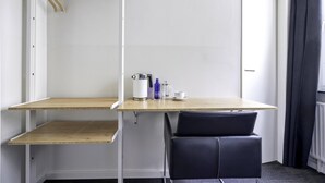 Una habitación pequeña y moderna con un escritorio de madera, una silla negra, una cafetera y una taza.