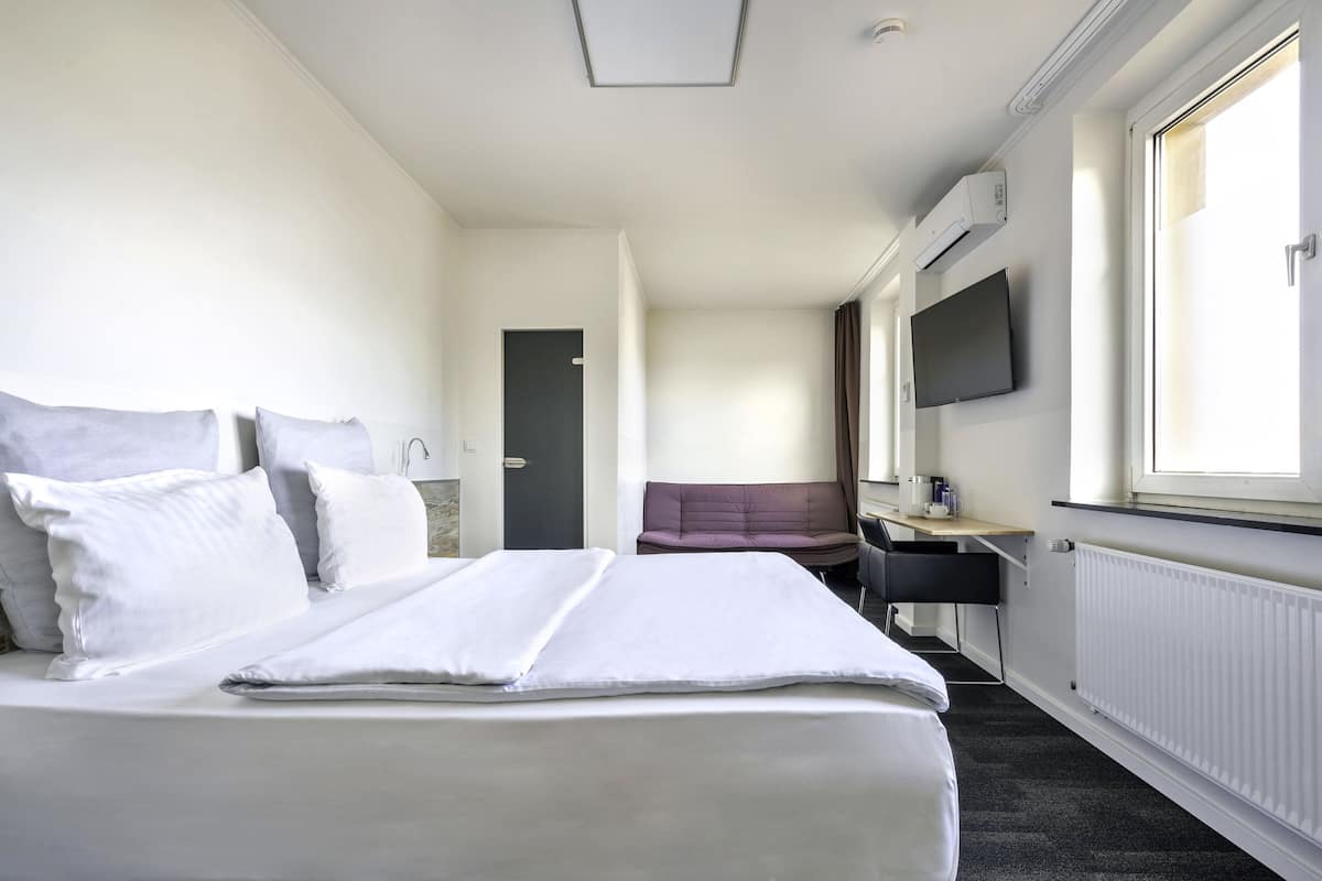 Une chambre d’hôtel avec un lit, un bureau, une chaise, une télévision et une fenêtre.