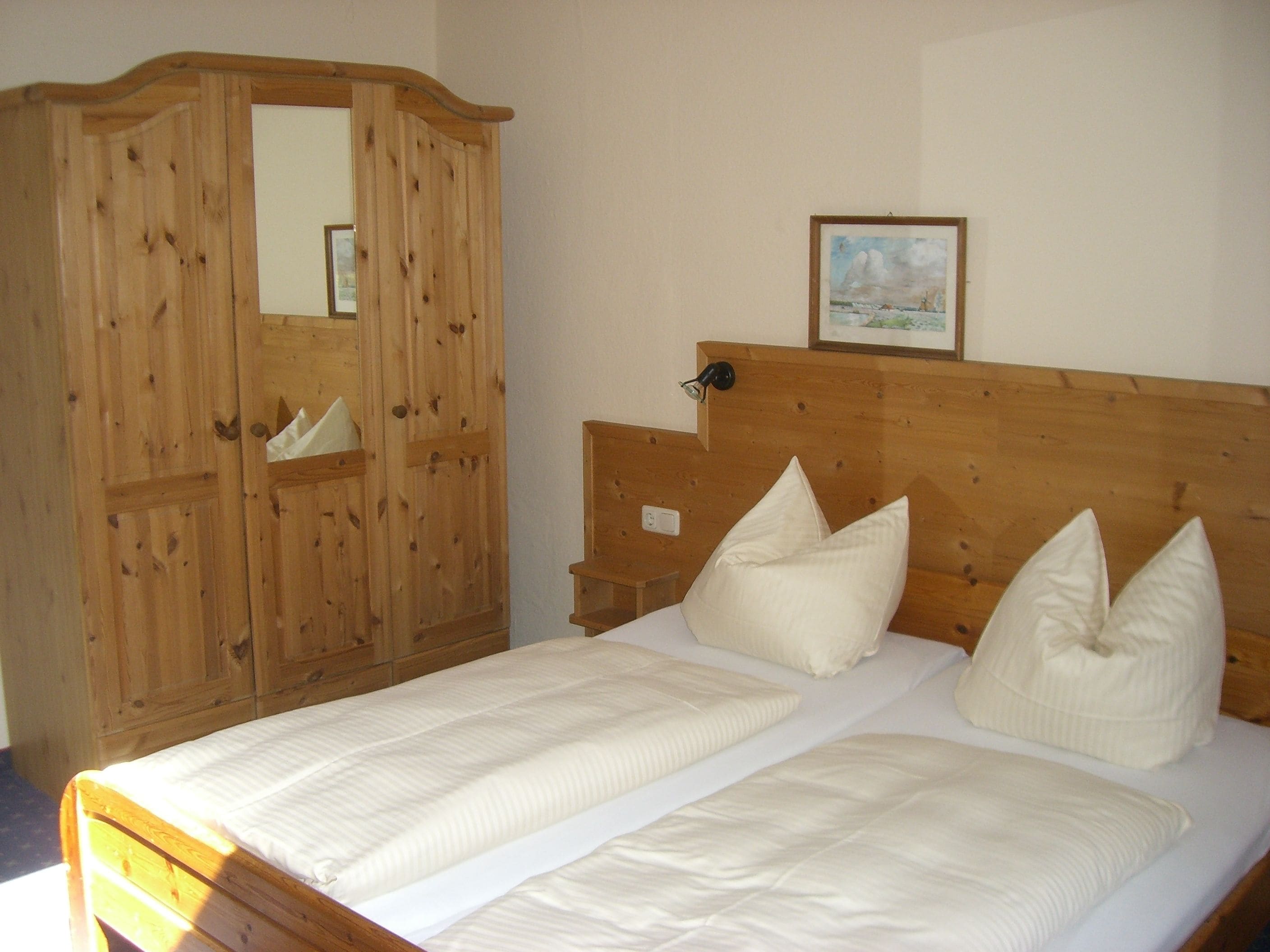 Un dormitorio con estructura de cama de madera, dos almohadas, una mesita de noche y un armario de madera con espejo.