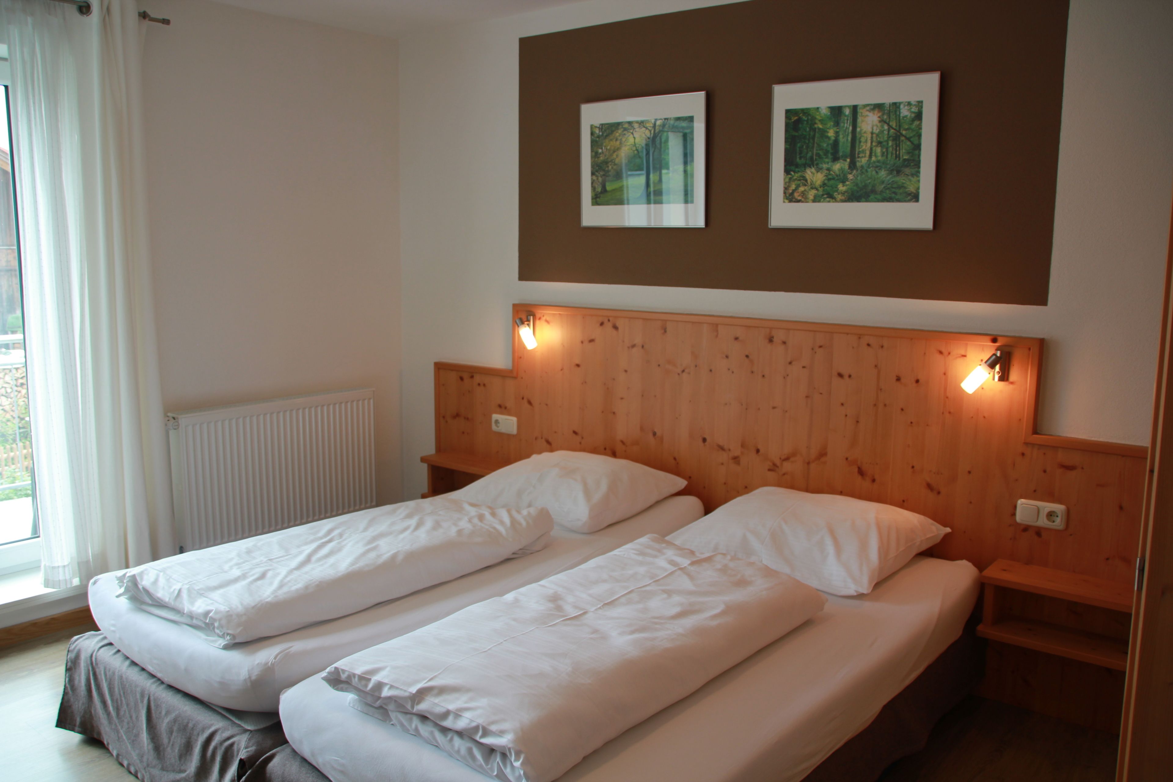 A bedroom with two single beds, wooden headboard, and two framed pictures on the wall.