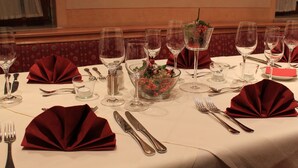 Ein Tisch, festlich gedeckt für ein formelles Abendessen, mit mehreren Weingläsern, einer Obstschale und roten Servietten.
