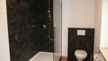Un baño moderno con ducha de mampara de vidrio, inodoro blanco y salpicadero de mármol.