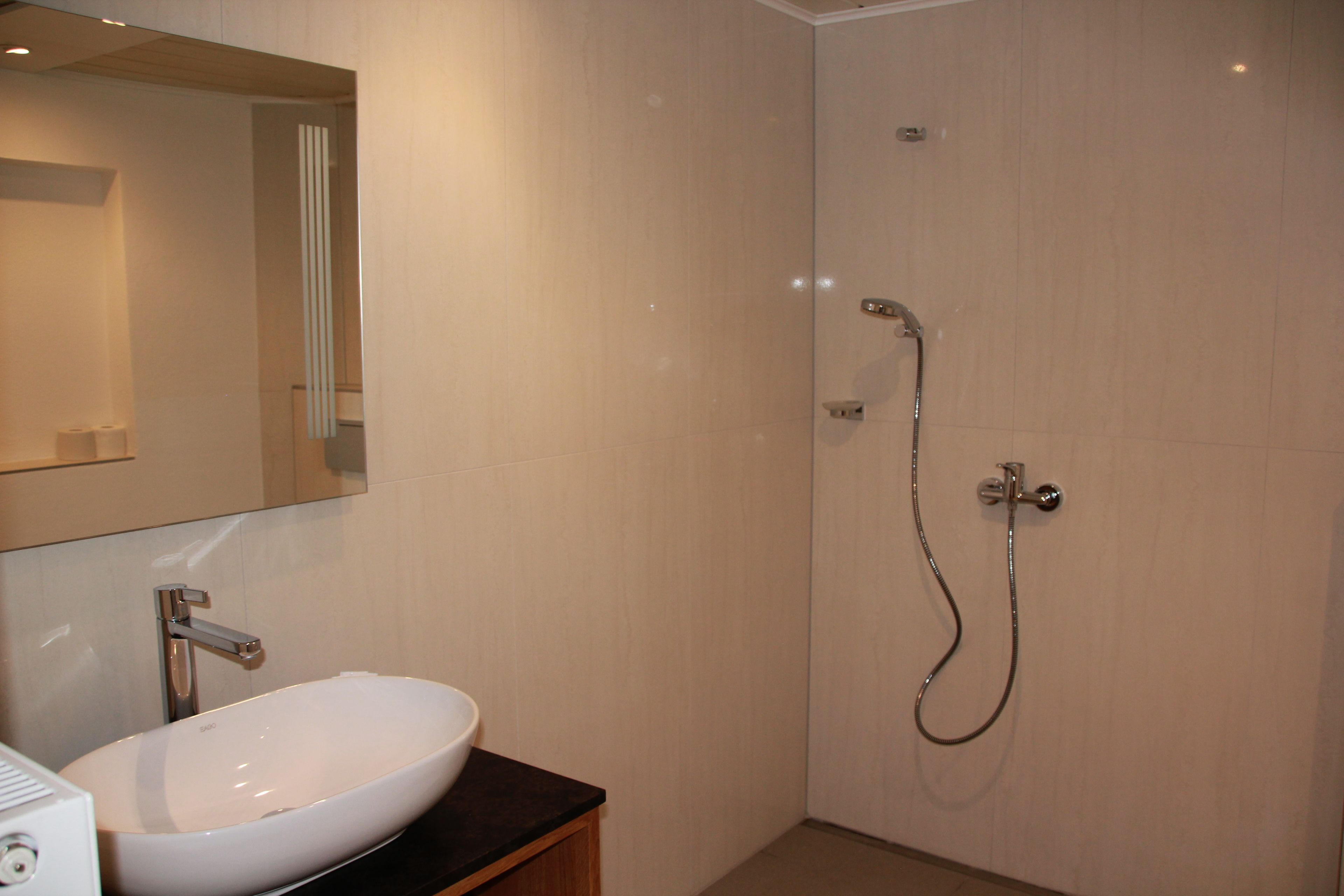 Un baño con lavamanos blanco, espejo y ducha.