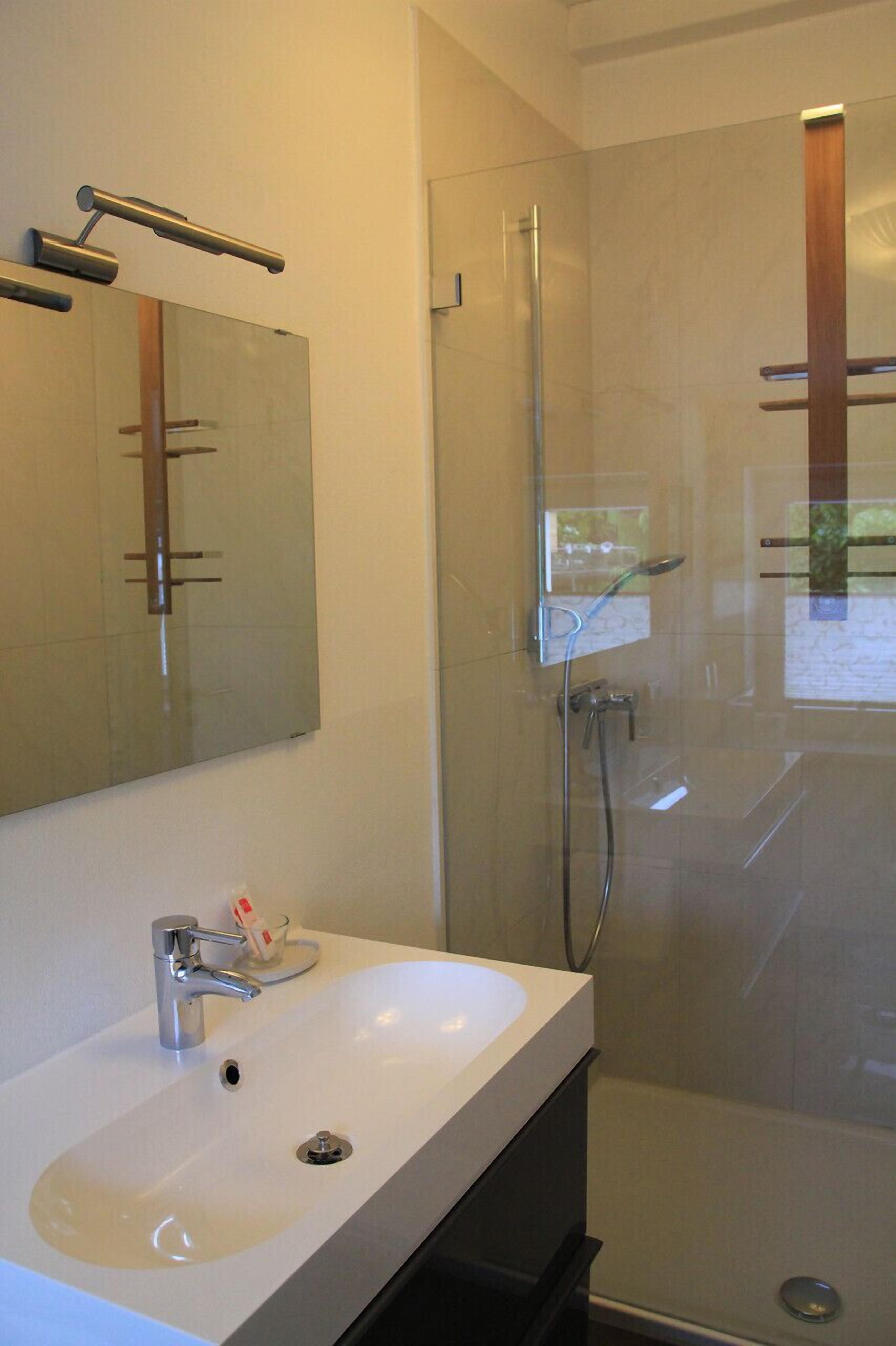 Une salle de bain moderne avec un lavabo blanc, un miroir, une cabine de douche en verre et un porte-serviettes.