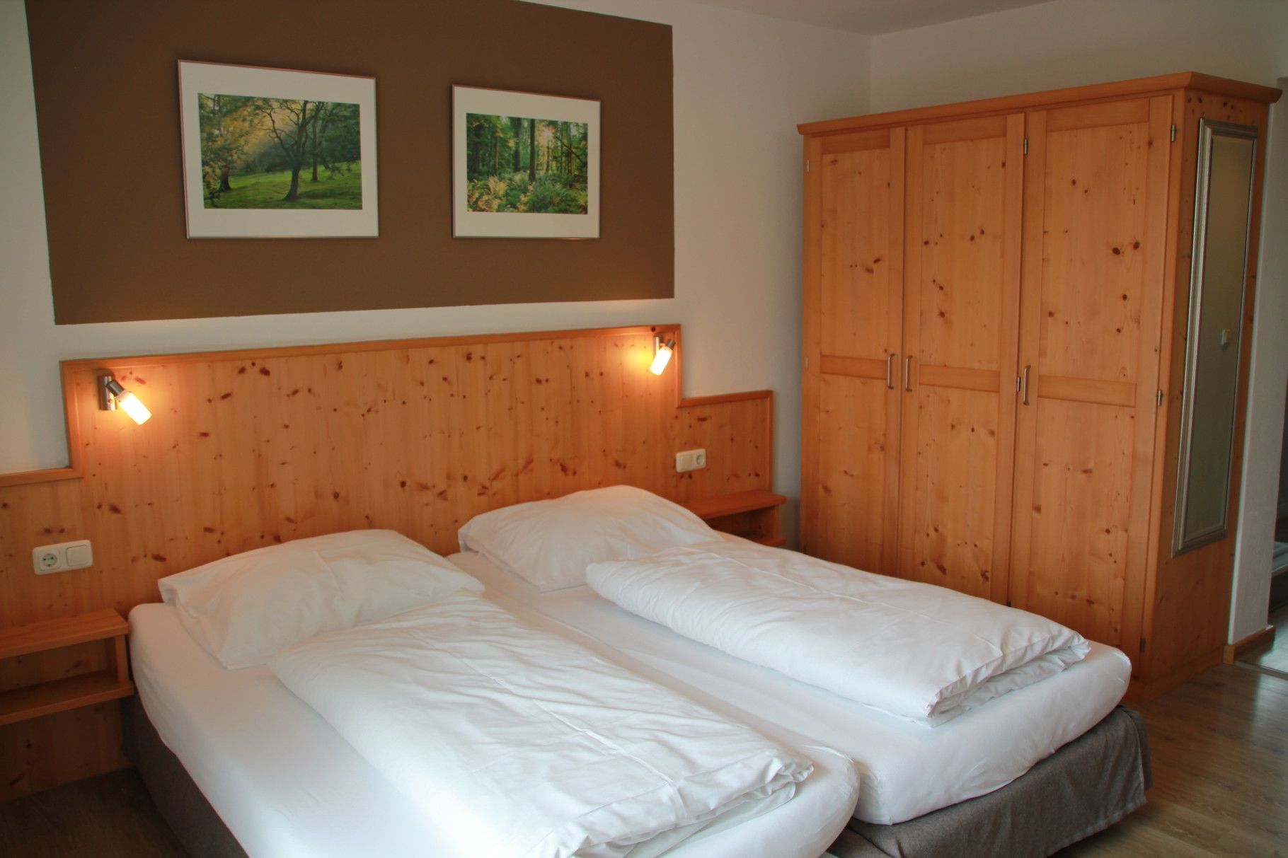A room with two single beds, wooden headboards, and a large wardrobe.