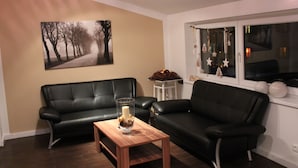 Ein Wohnzimmer mit zwei schwarzen Ledersofas, einem Couchtisch mit Kerze und einem großen gerahmten Bild an der Wand.