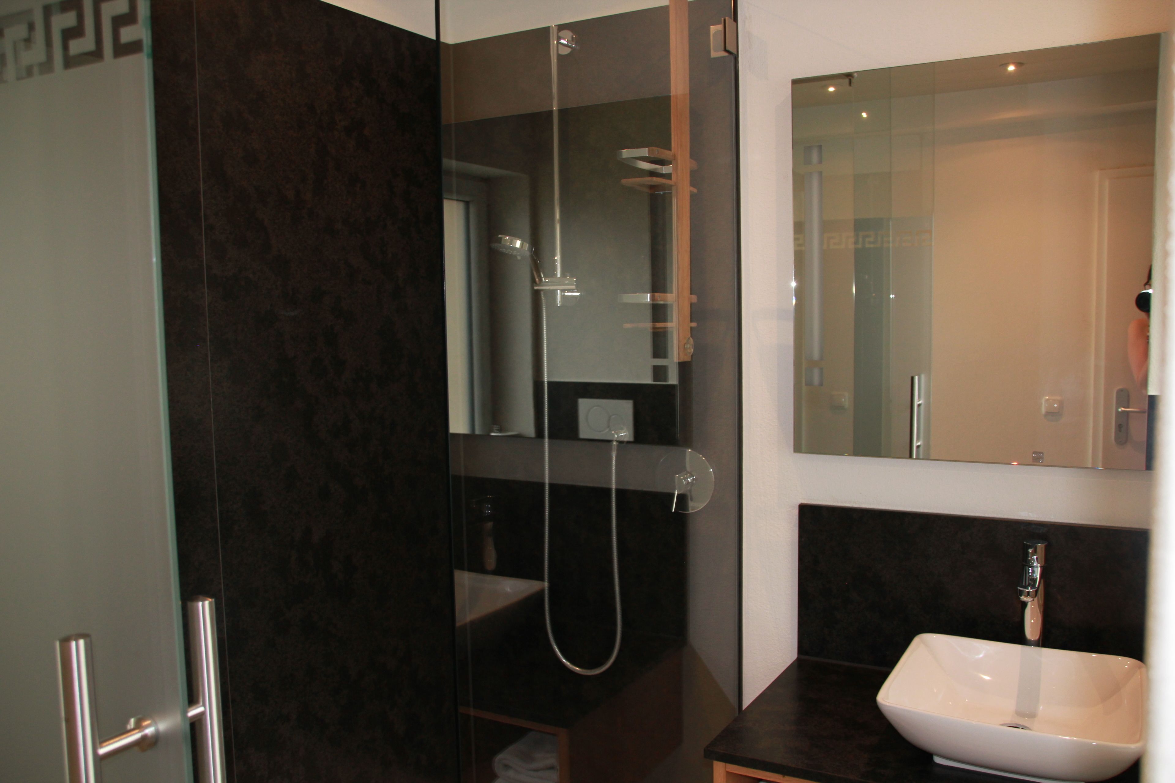 A modern bathroom with a glass-enclosed shower, a white sink, and a large mirror.