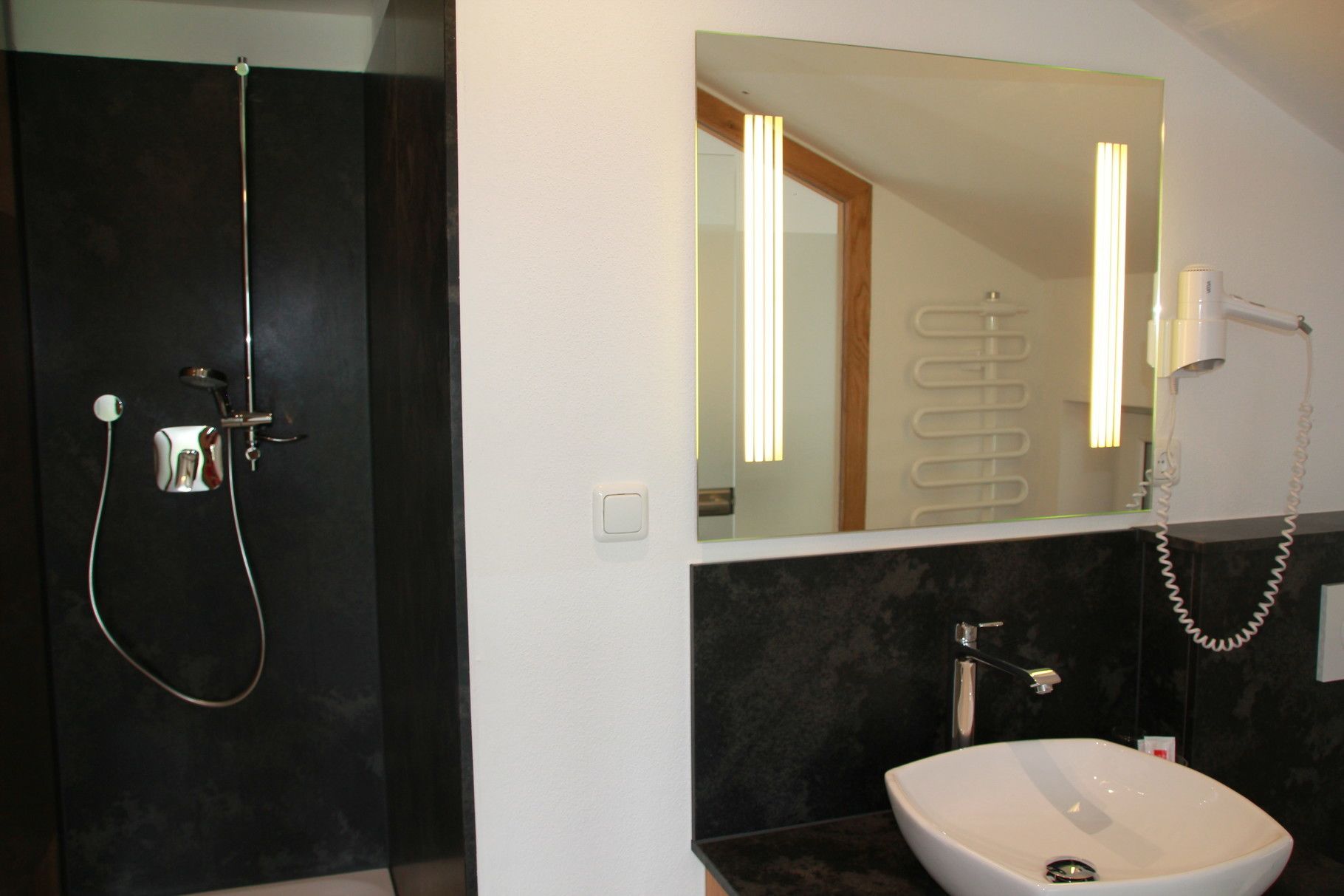 A modern bathroom with a dark shower enclosure, a large mirror, and a white sink.