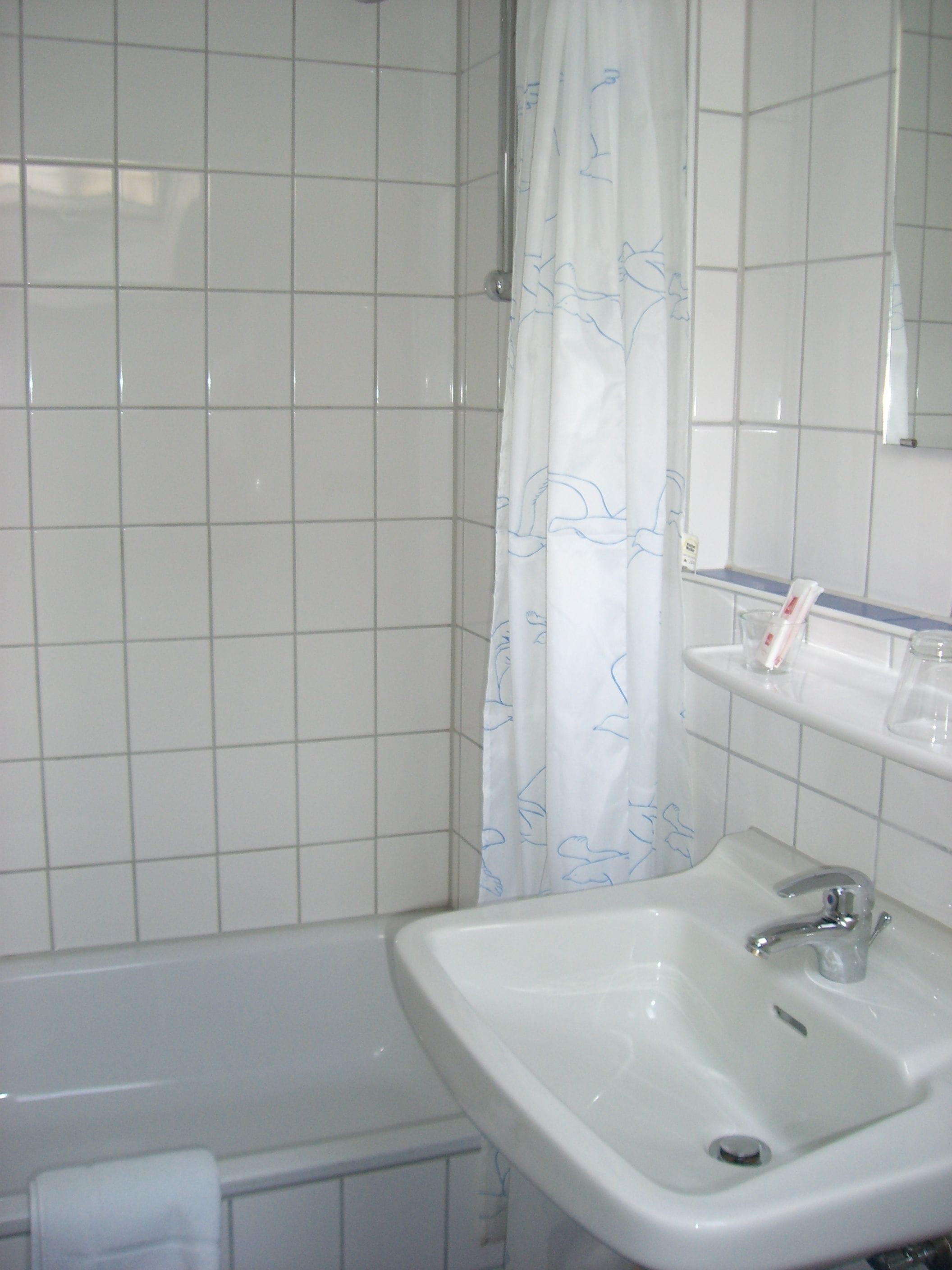 A bathroom with a white bathtub, a sink with a mirror above it, and a shower curtain with a blue pattern.