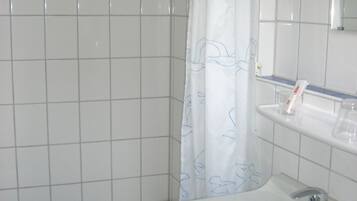 A bathroom with a white bathtub, a sink with a mirror above it, and a shower curtain with a blue pattern.