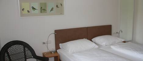 A bedroom with a single bed, a chair, and a wall-mounted picture of birds.