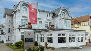 A historic hotel with a classic European architectural style, featuring multiple balconies and a prominent red flag.