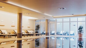 A spa area with a large indoor pool, lounge chairs, and a potted plant.