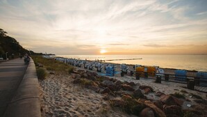 A beachside walkway with beach chairs and umbrellas, a sandy path, and a rocky shoreline.