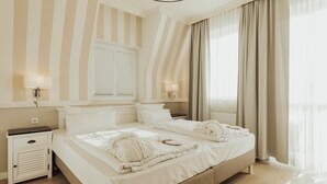 A double bed with white linens, a bedside table, a lamp, and a window with curtains.