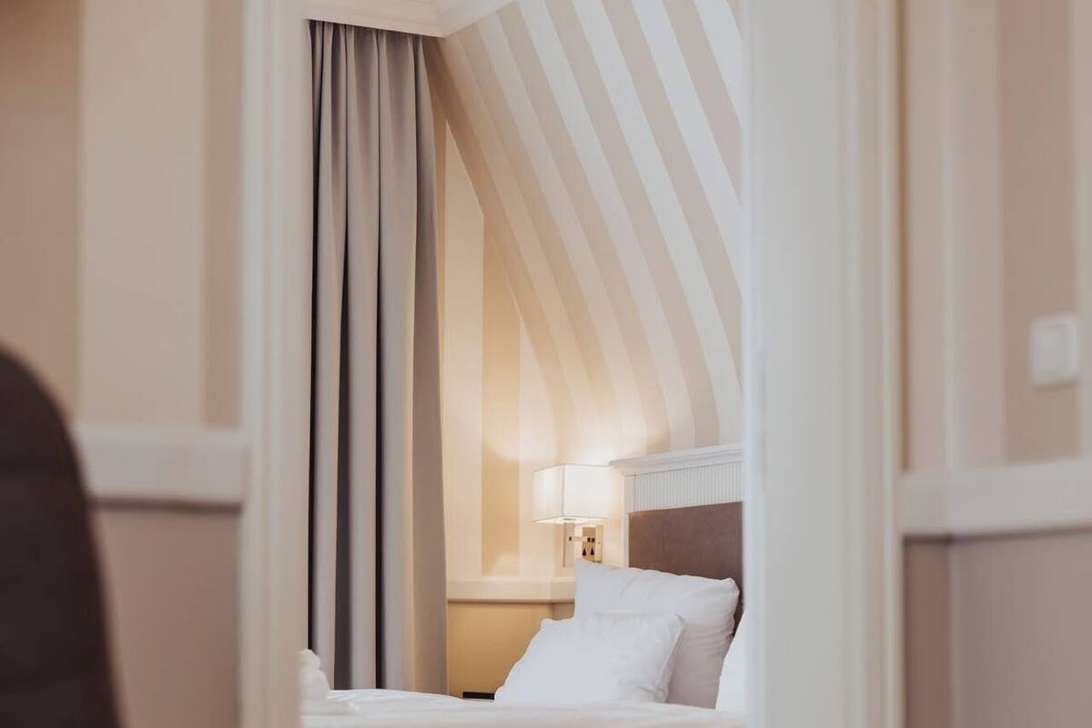 Une chambre d’hôtel avec un lit, une table de chevet avec une lampe et une vue sur l’extérieur par une fenêtre munie de rideaux.