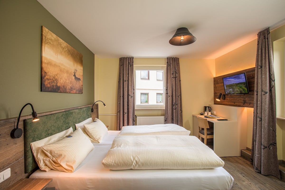 Een hotelkamer met twee bedden, een bureau, een televisie en een schilderij aan de muur.
